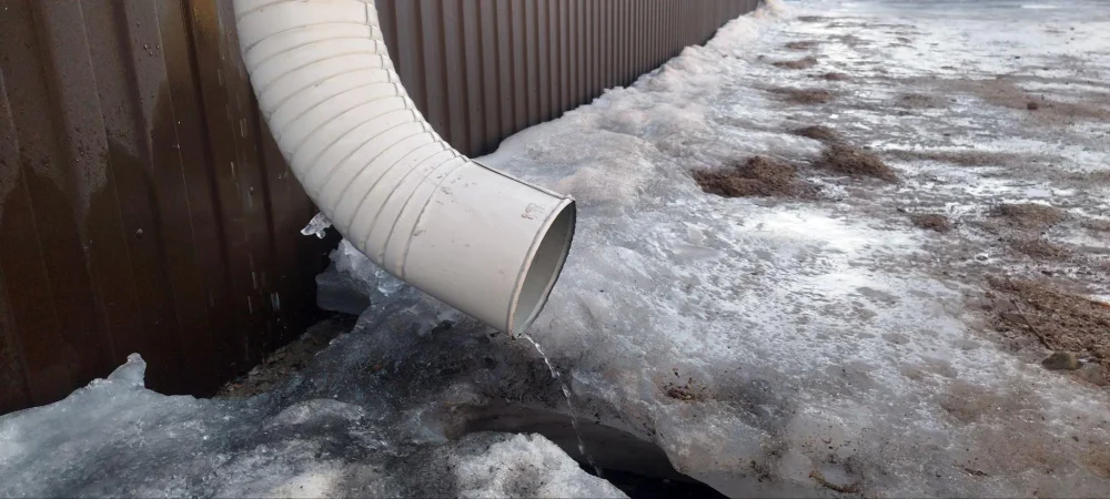 Frozen downspout outlet with ice buildup near drainage area